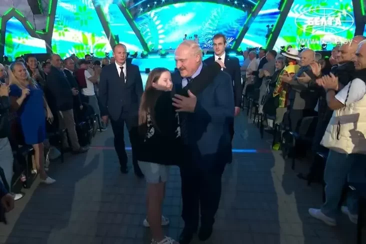 Nikołaja Łukašienko i nieopoznannyj tiełochranitiel soprovoždajut Aleksandra Łukašienko v tołpie. Aleksandrija, Mohilevskaj obłasť, ijul 2024 hoda. Skrinšot: Informacionnoje ahientstvo BiełTA, YouTube